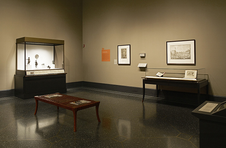 Fig. 3. Installation view of the exhibition's right side: left background, case with Etruscan small bronzes; middleground, bench with catalogues; center background, wall-mounted case with ancient coins; right background, 16th–18th-century illustrated books, an engraving, and a manuscript documenting the Chimaera of Arezzo's western afterlife (E.M. Rosenbery).